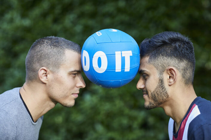 Foto: Zwei Junge Männerköpfe mit einem Ball in der Mitte, Teamkoordinater Balazs Petik mit Bilal