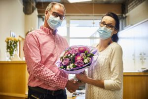Foto: Einrichtungsleiter vom Haus Simeon gratuliert Mitarbeiterin mit Blumenstrauß